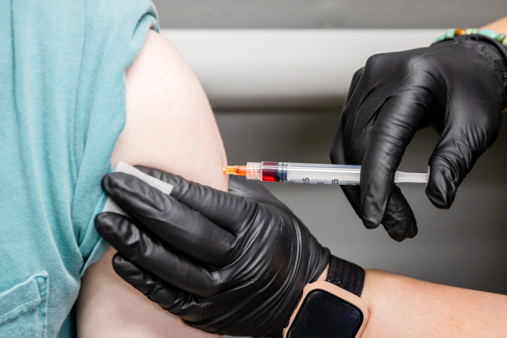 A Lume provider's hands in black medical gloves delivers an injection of vitamins into a client's upper arm. The supplement also includes glutathione in River North, Chicago.