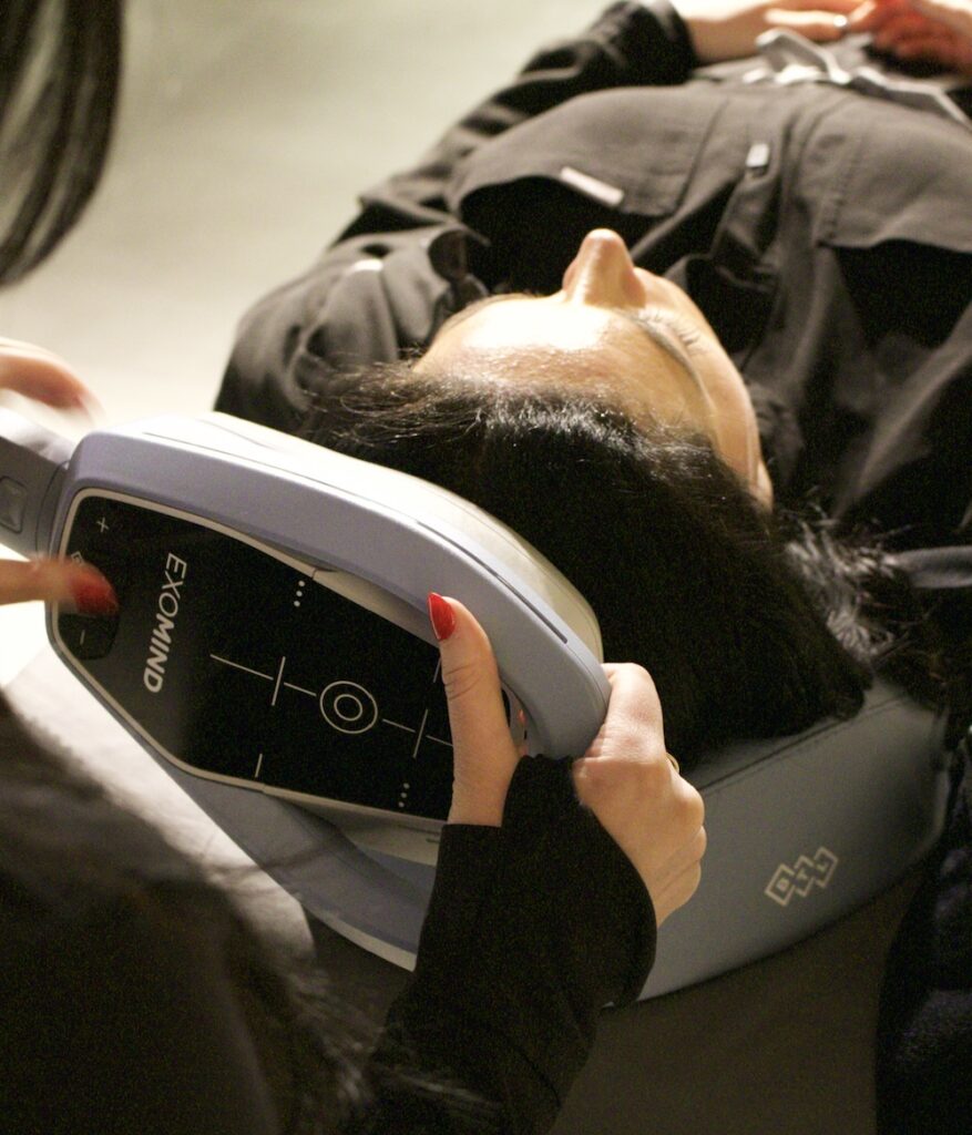 Female patient lying on her back in a treatment room as her provider places the ExoMind applicator on her head. This is a treatment for binge eating support in River North, Chicago.